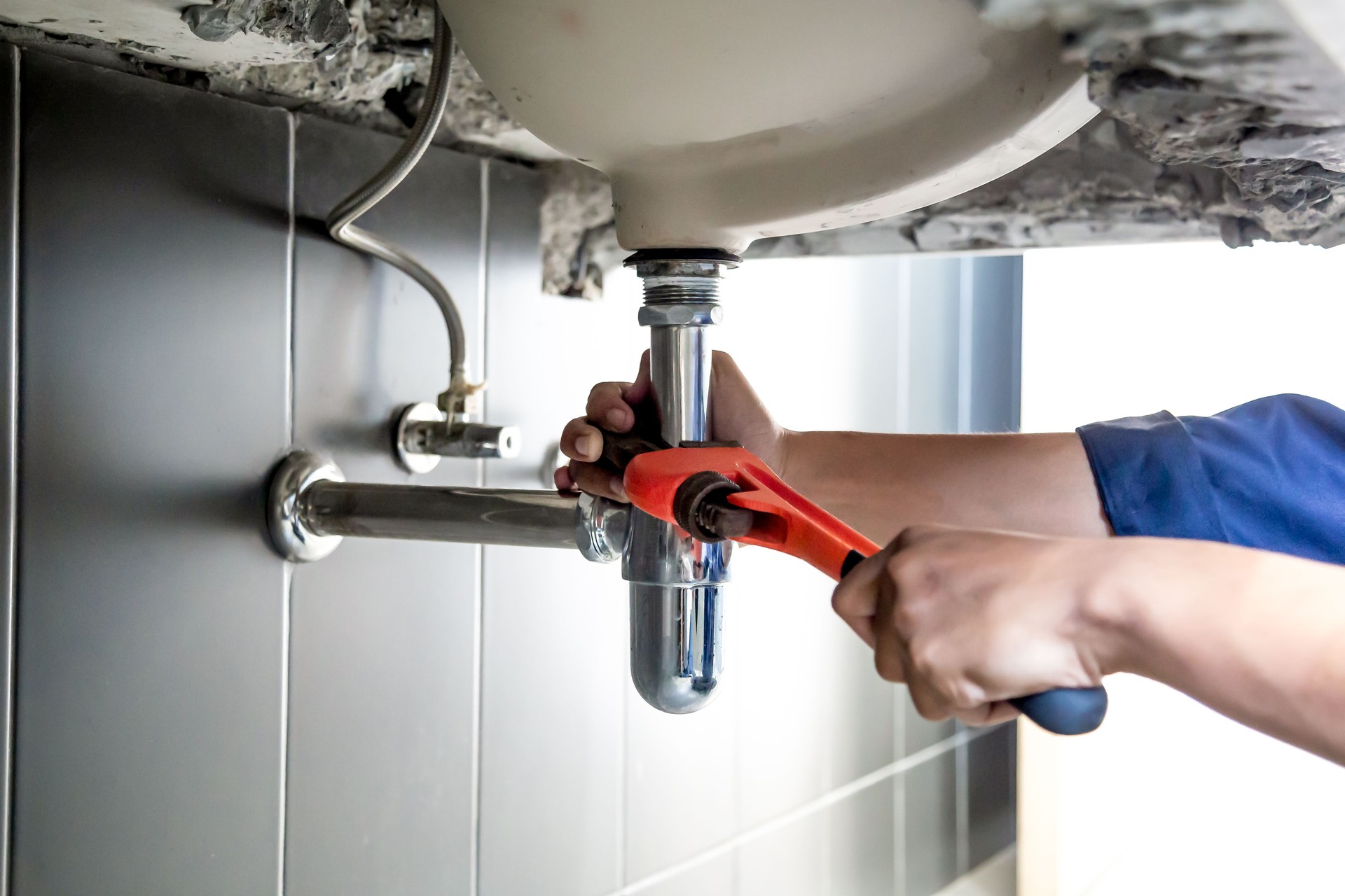 Plumber uses wrench to repair water pipe under sink There is maintenance to fix the water leak in the bathroom.with red wrench, plumbing install concept.